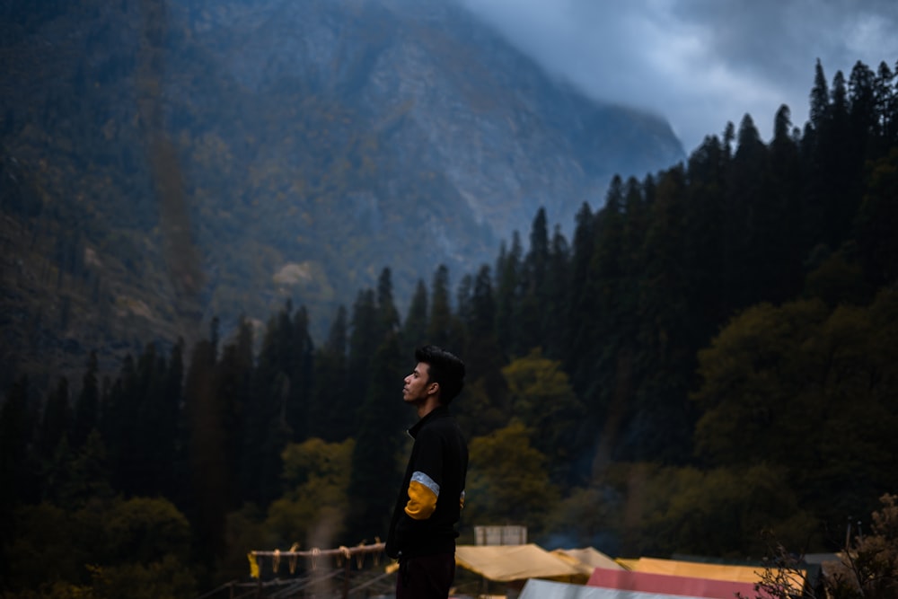 man in black jacket standing on brown wooden fence during daytime