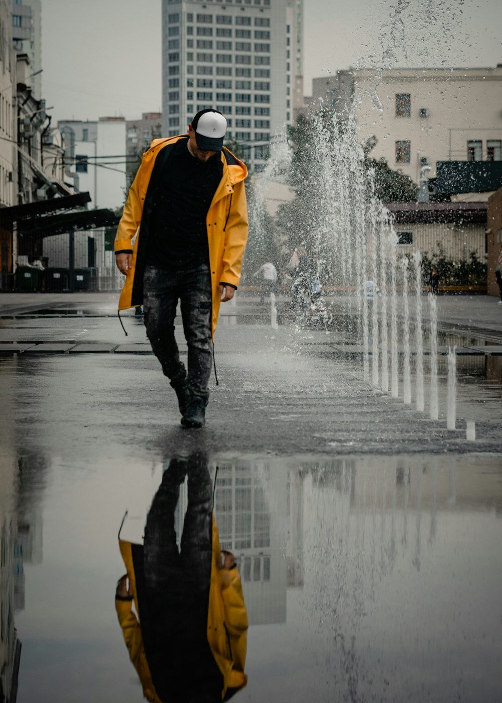 Hombre en chaqueta amarilla y pantalones negros de pie en la fuente de agua durante el día