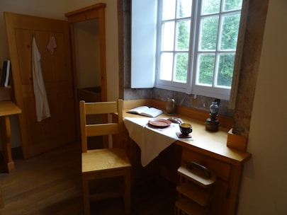 A cozy student hostel room with study desk and bed near a window.