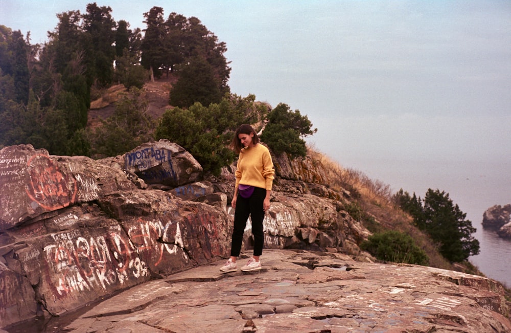 노란 셔츠와 검은 바지를 입은 남자가 낮에 바위 언덕에 서 있다