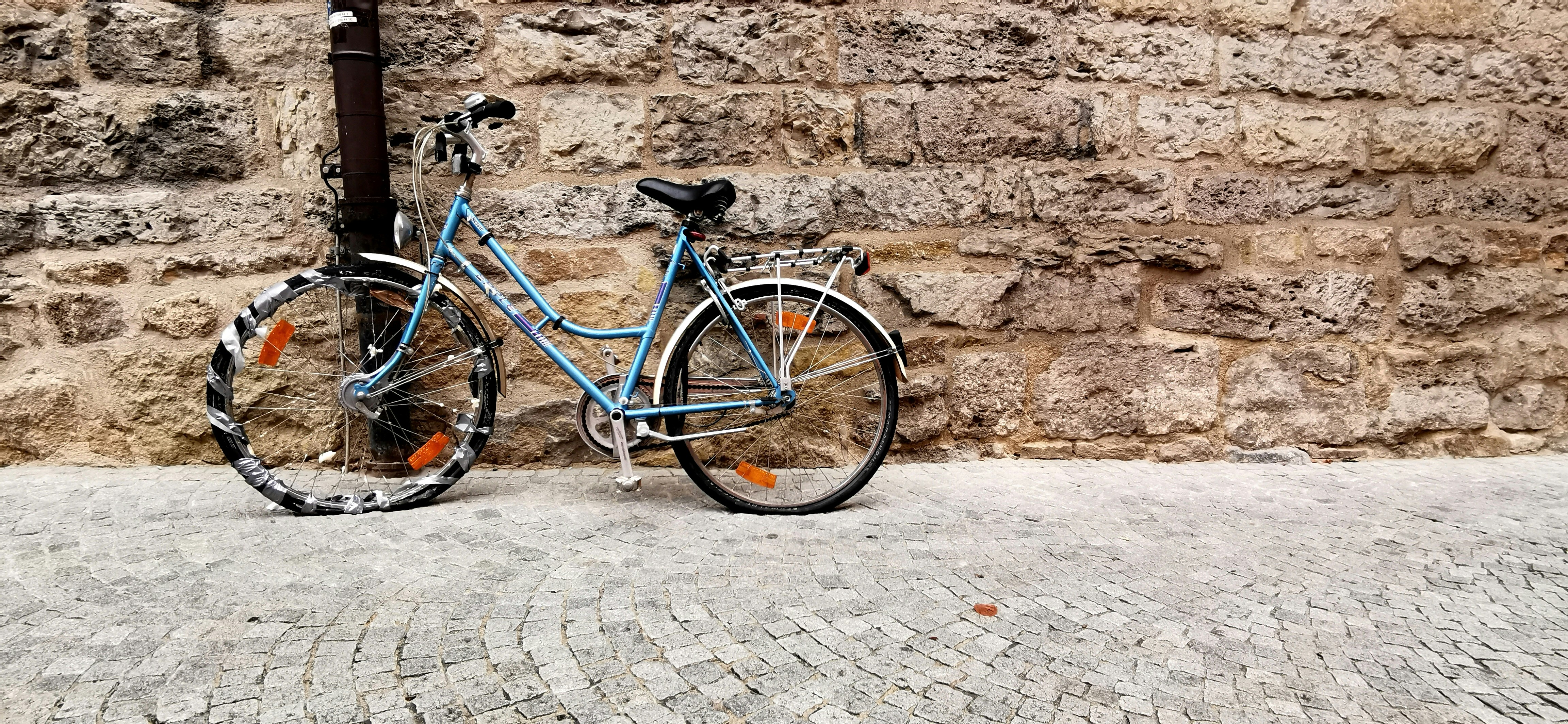 blue city bike parked beside brown brick wall