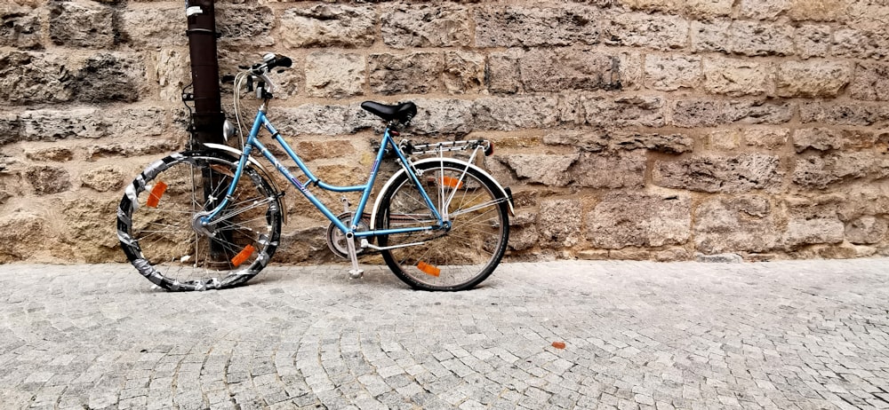 blue city bike parked beside brown brick wall