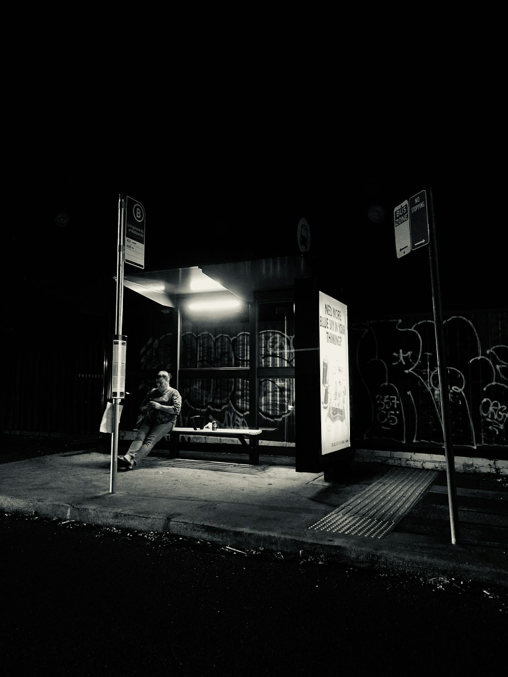 Mann in schwarzer Jacke und Hose sitzt nachts auf der Bank in der Nähe der Straßenlaterne