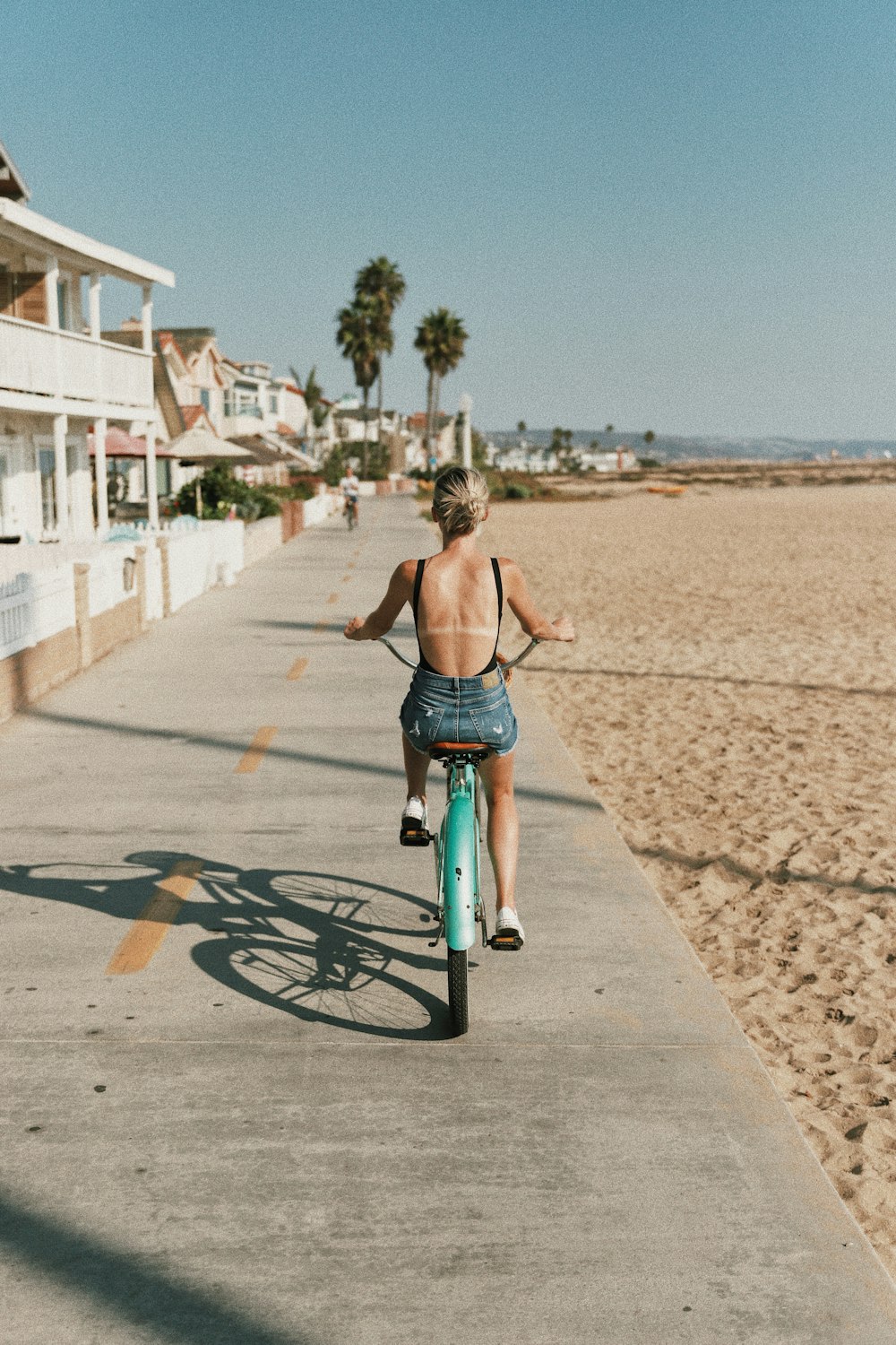 woman in black spaghetti strap top and blue denim jeans riding on black bicycle during daytime