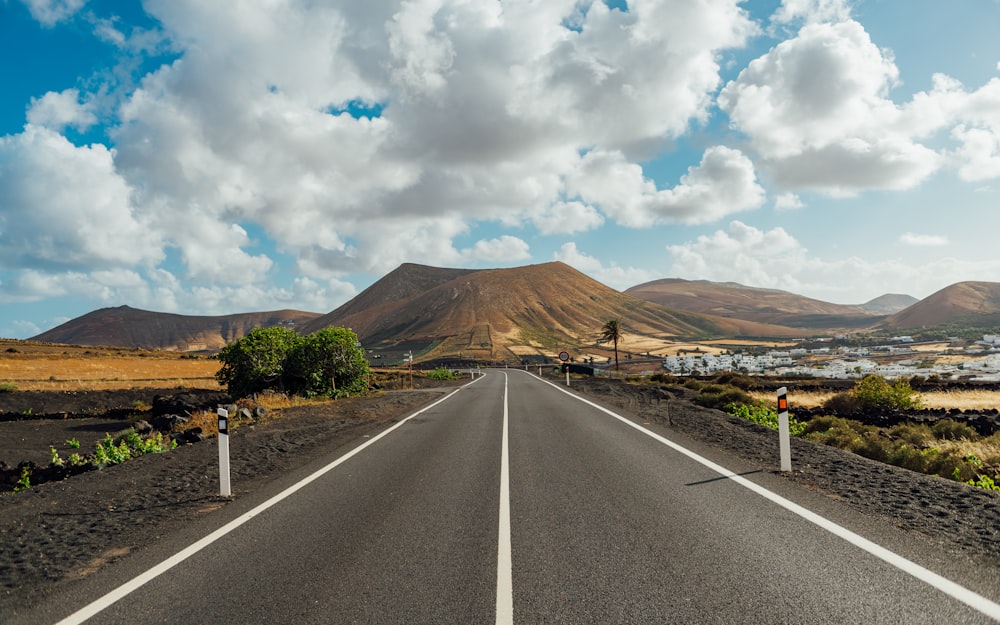 Carretera de asfalto gris cerca de la montaña marrón bajo nubes blancas y cielo azul durante el día