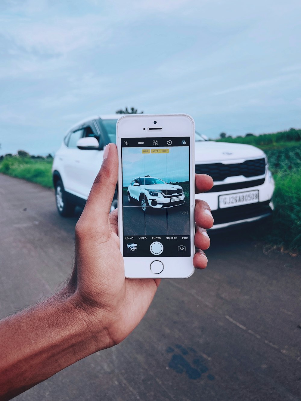 person holding silver iphone 6 taking photo of white car on road during daytime