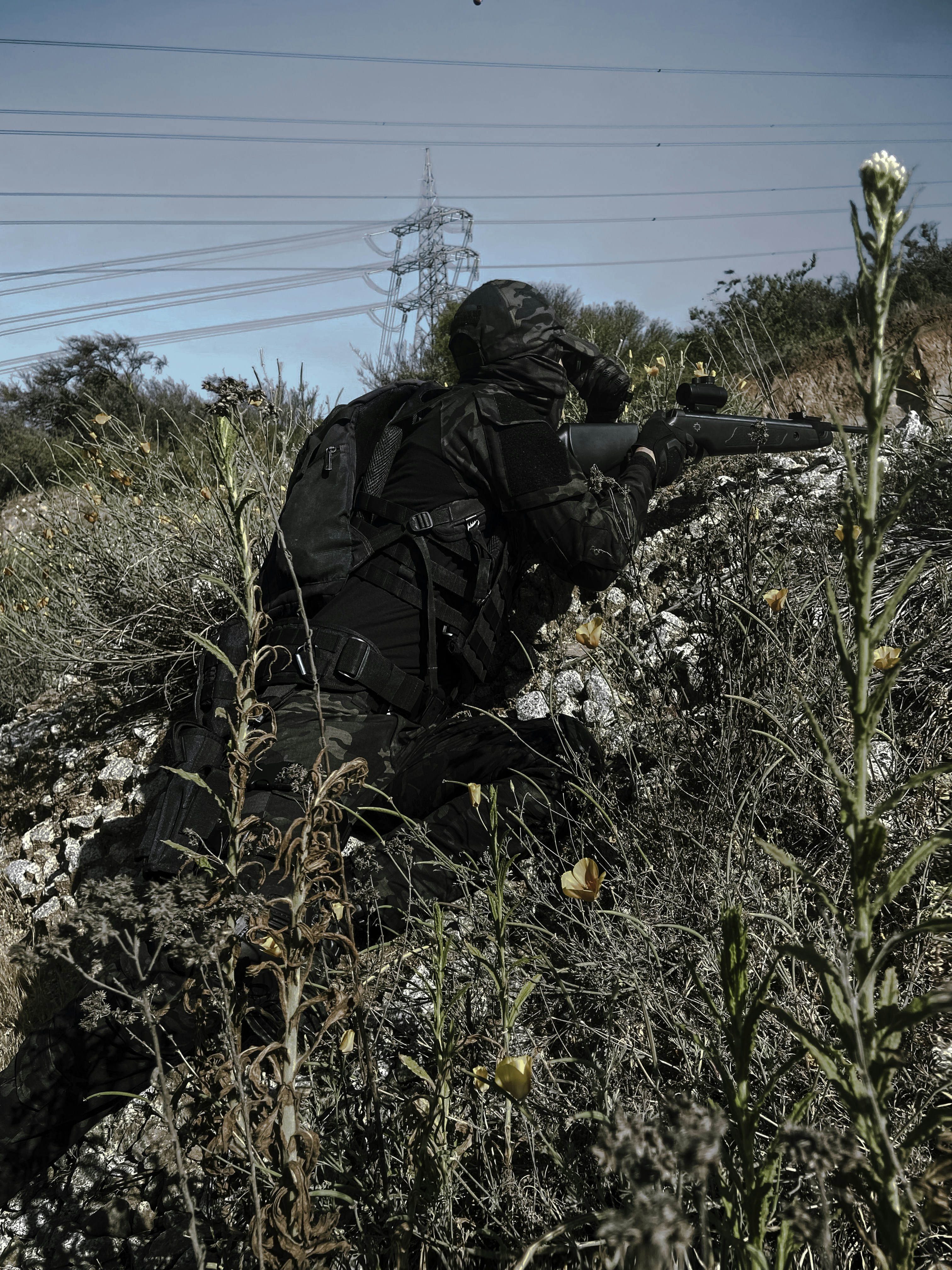 man in black jacket and black pants sitting on ground with yellow flowers during daytime
