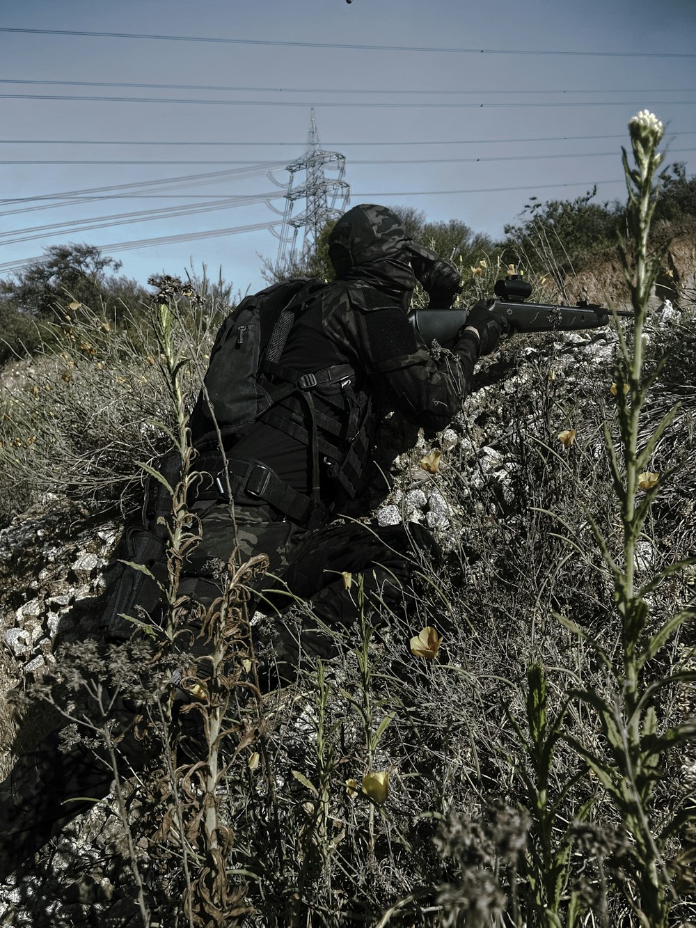 man in black jacket and black pants sitting on ground with yellow flowers during daytime