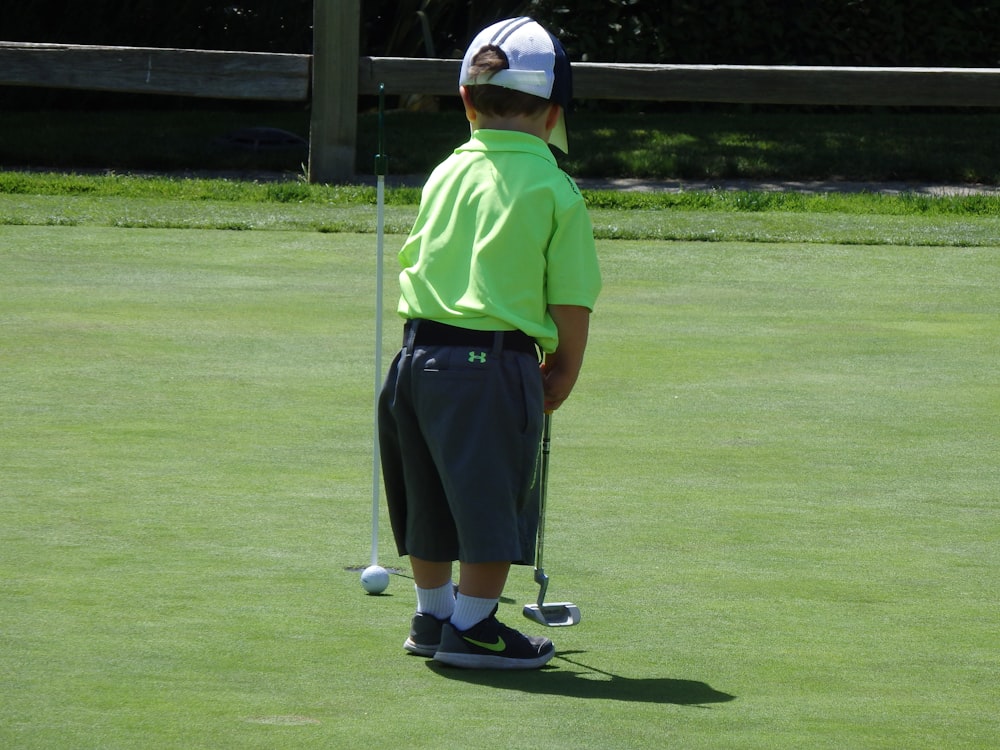 man in green polo shirt and black pants standing on green grass field during daytime