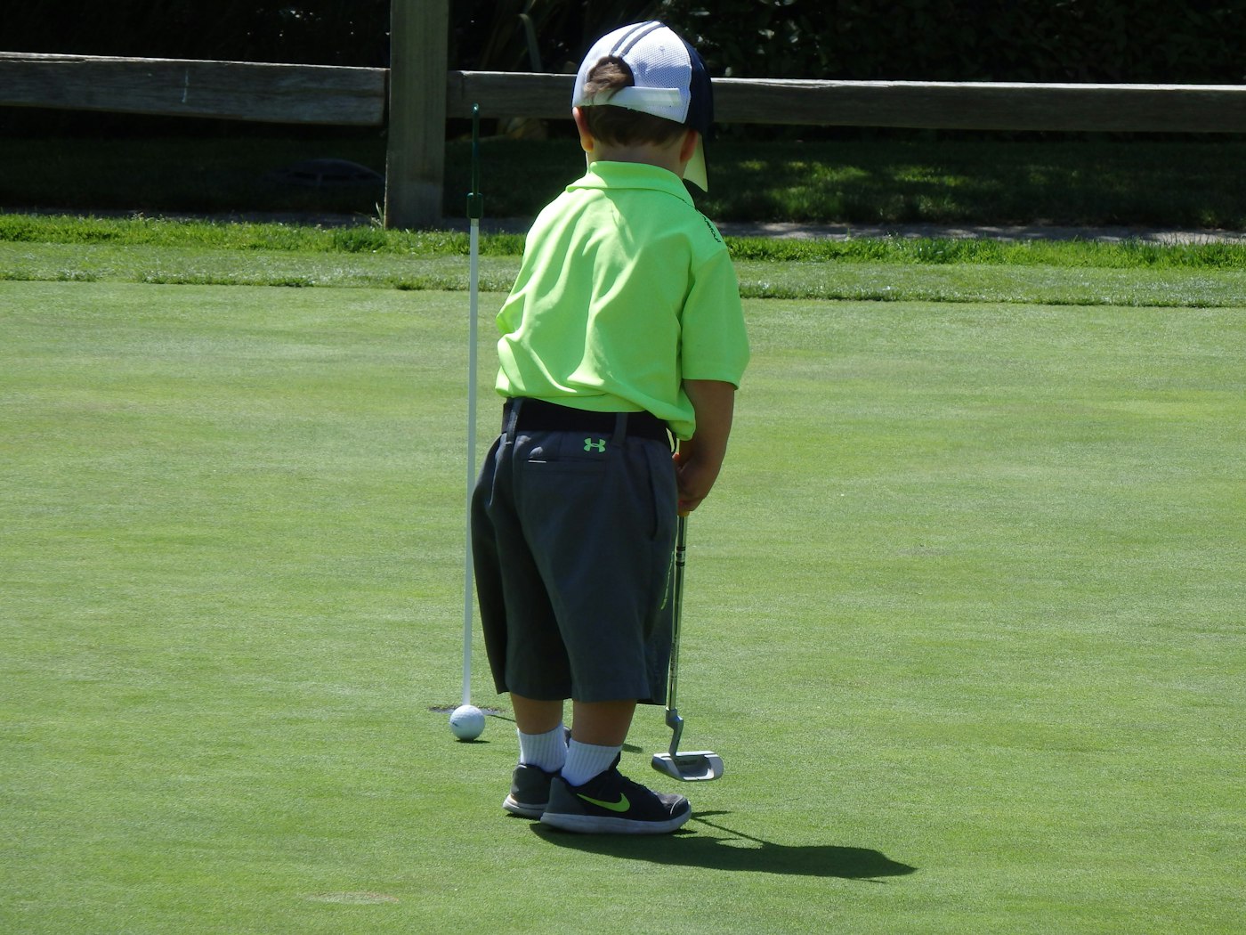 Enfant s'initiant au golf en famille sur le green