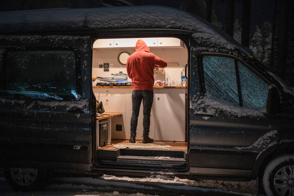 man in red hoodie standing in front of white and black car door