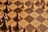 A chessboard with alternating light and dark brown squares is shown, featuring several wooden chess pieces. The pieces include pawns and other pieces forming a game setup but not arranged in a starting position. A combination of light-colored and dark-colored chess pieces are present.