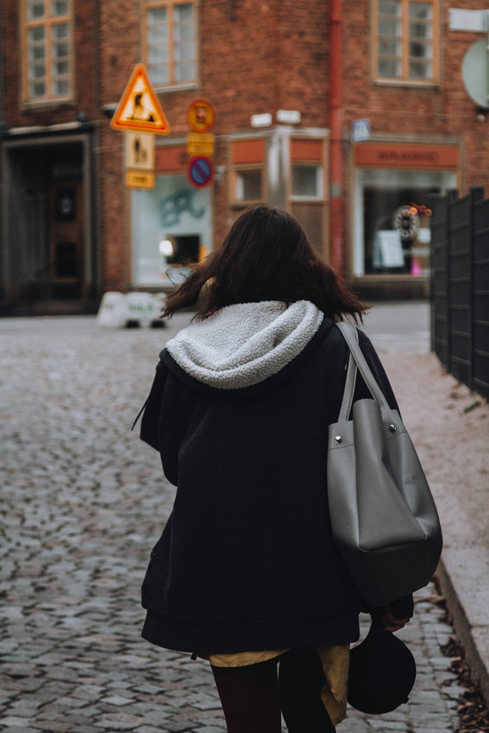 woman in black jacket walking on sidewalk during daytime