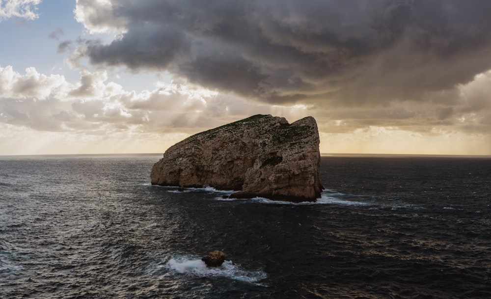 brown rock formation on sea under gray clouds