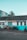 Several motorcycles are parked in front of a building with a sign reading 'Alan Lear Motorcycles'. The building is painted white and turquoise with large windows, and the sign also mentions services like MOTs, sales, service, and parts. The sky is clear and blue, suggesting a bright day.