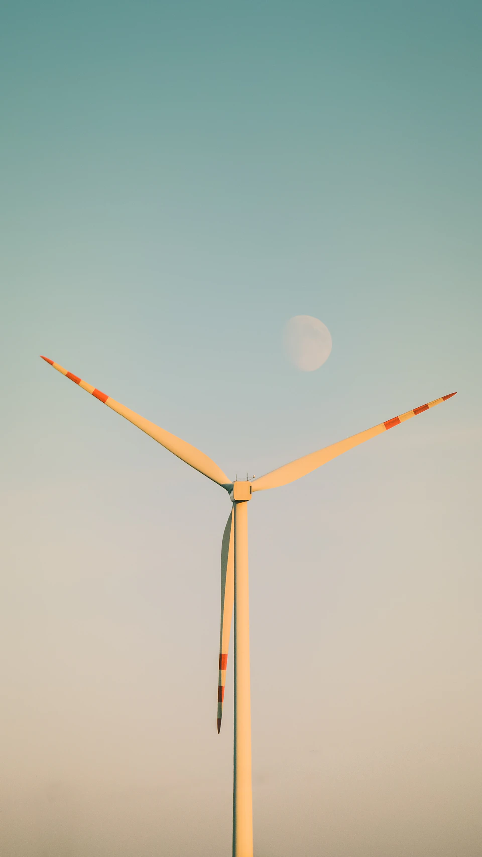 Large white wind turbine stands tall against clear blue sky with crescent moon visible