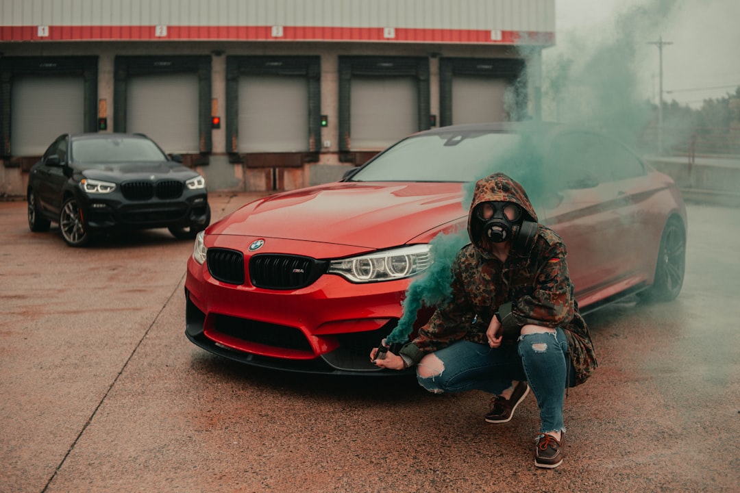 man in black leather jacket and blue denim jeans sitting on red bmw car