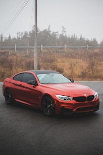 A sleek red sports car parked on a textured asphalt road under moody evening light.