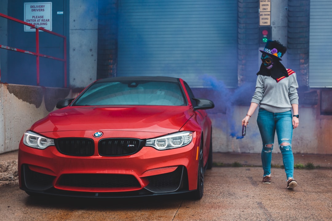 woman in white t-shirt and blue denim jeans standing beside red bmw car