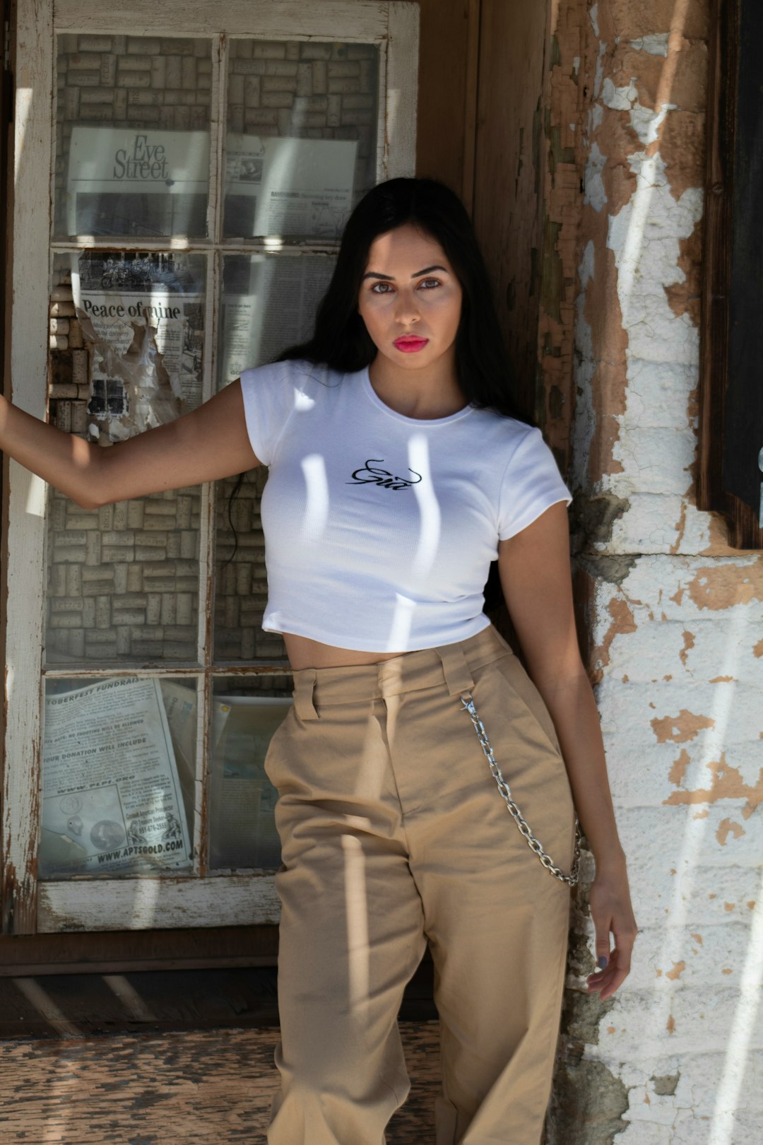 woman in white crew neck t-shirt and brown pants standing beside brown brick wall