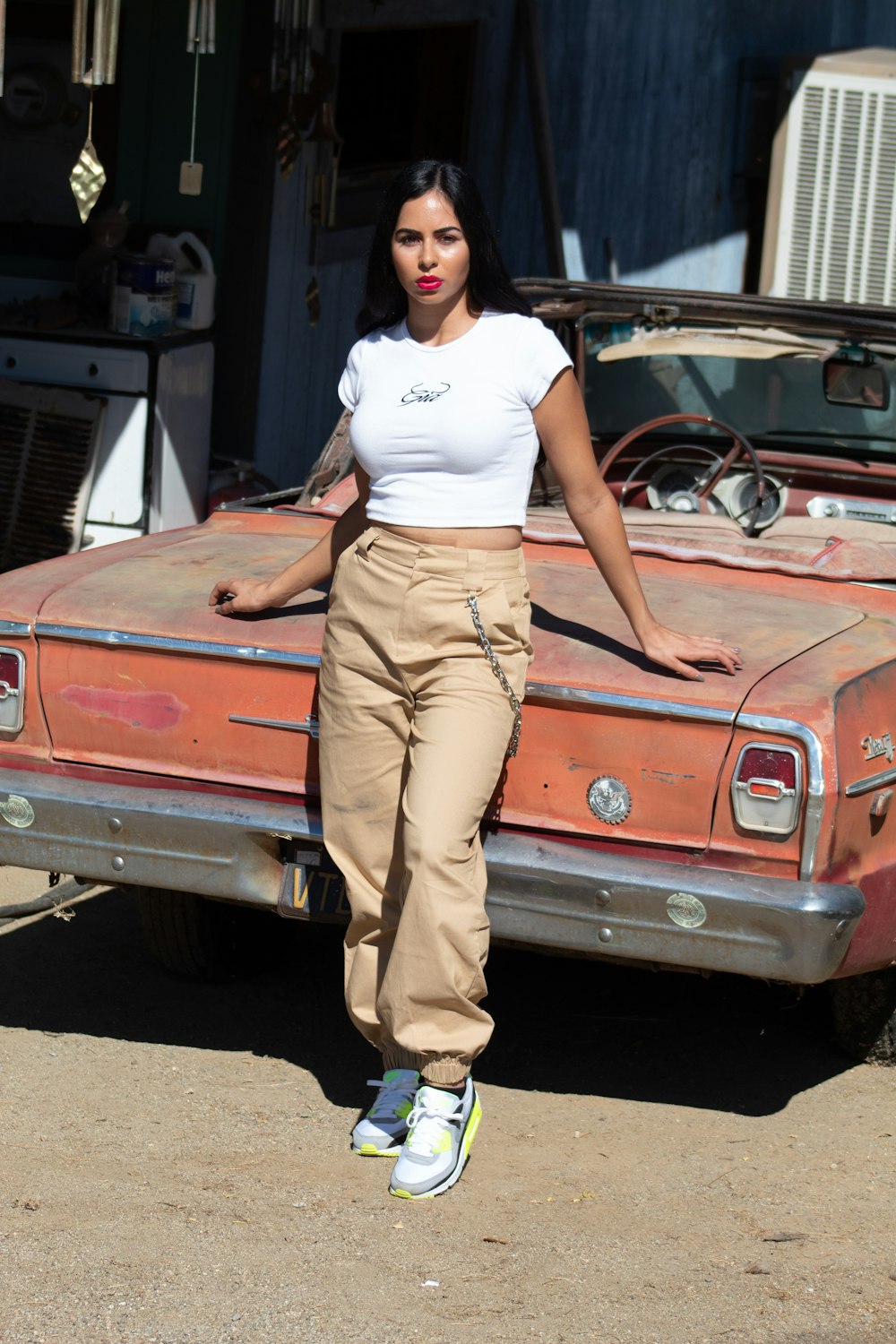 woman in white t-shirt and brown pants leaning on brown car