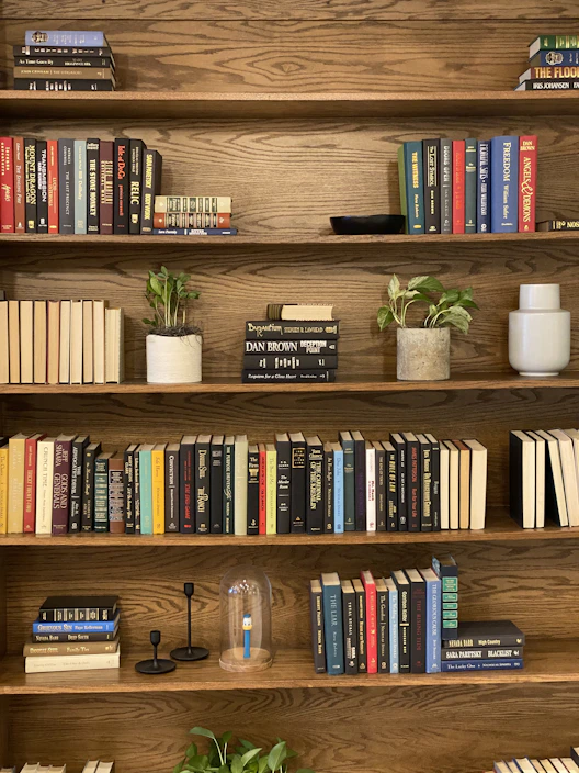A sturdy wooden bookcase filled with books and small plants, showcasing natural wood grain.