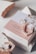 A beauty product box is displayed with stylish packaging. It includes elements like a circular metal accessory, a rose quartz crystal, and pink tortoiseshell-style earrings. The box features text promoting the product's natural and detoxifying properties, and it's set against a backdrop of textured materials.