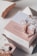 A beauty product box is displayed with stylish packaging. It includes elements like a circular metal accessory, a rose quartz crystal, and pink tortoiseshell-style earrings. The box features text promoting the product's natural and detoxifying properties, and it's set against a backdrop of textured materials.