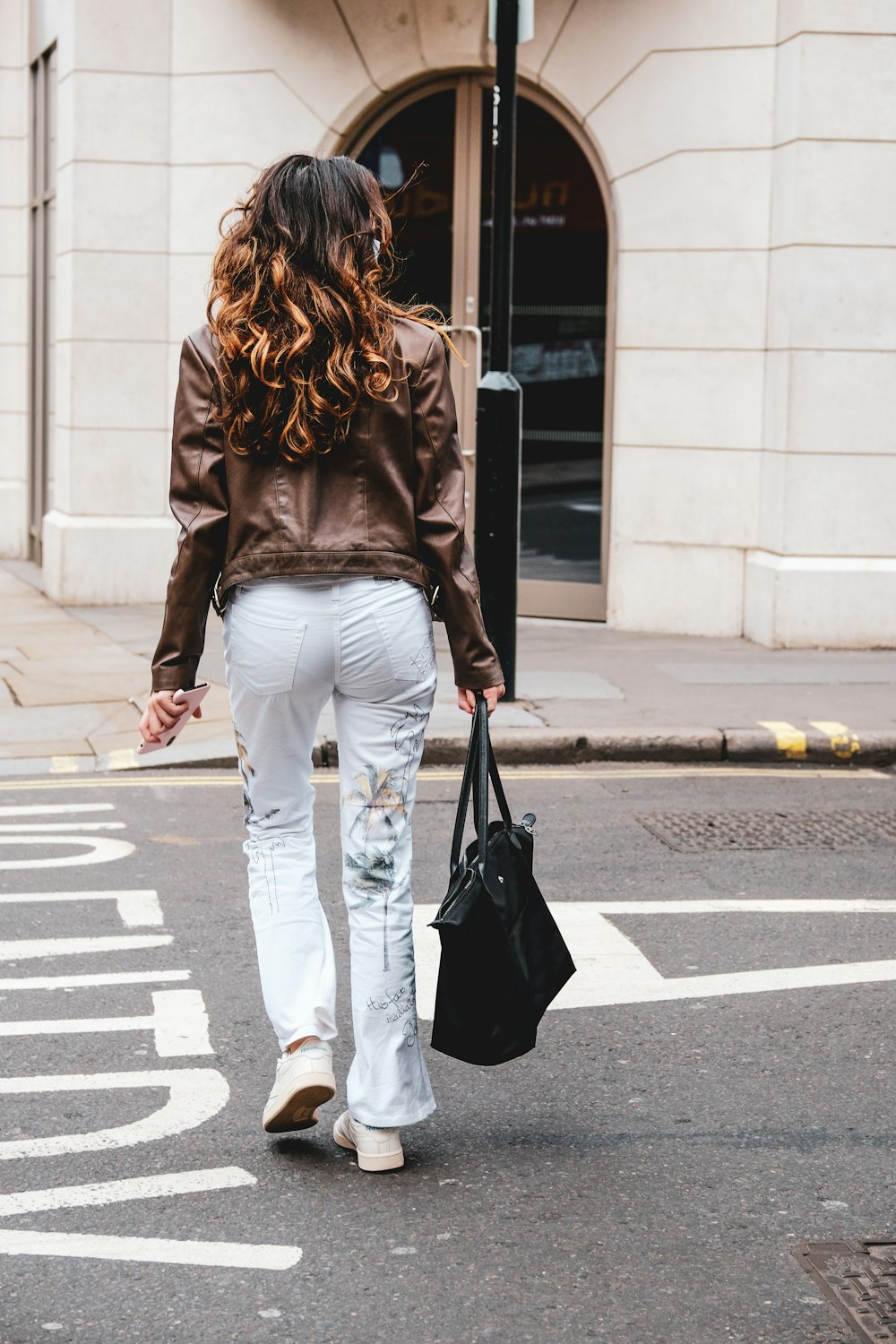 woman in black long sleeve shirt and white pants walking on pedestrian lane