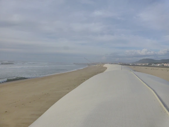 A team of engineers examining shoreline erosion with measuring instruments on a sandy beach at sunrise
