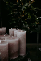 Close-up of hand-poured candles with subtle gold accents surrounded by textured fabrics and sage green leaves.