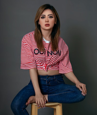 woman in red and white striped shirt and blue denim jeans sitting on gray chair