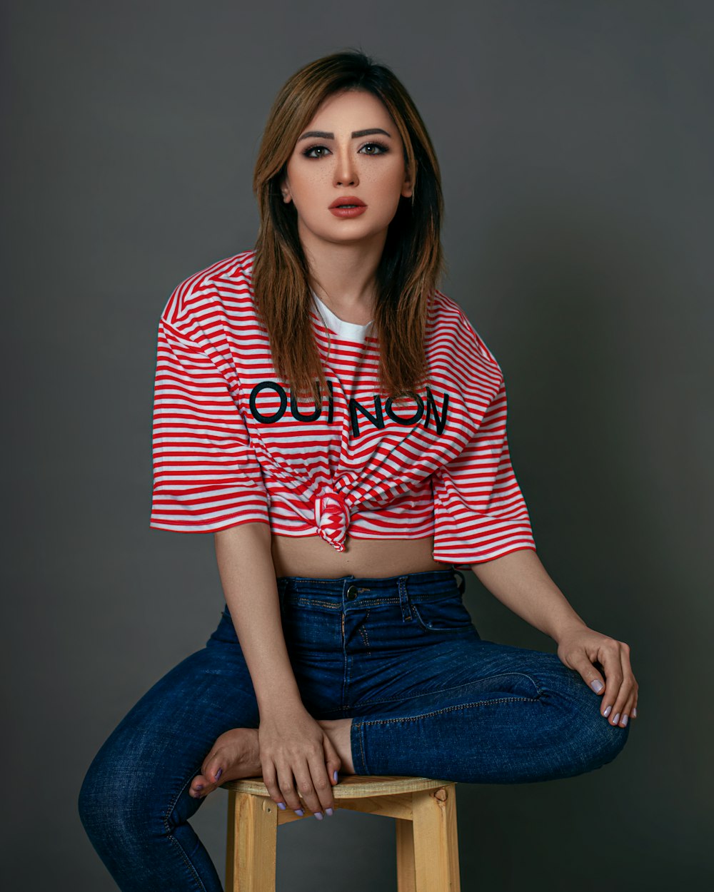 woman in red and white striped shirt and blue denim jeans sitting on gray chair