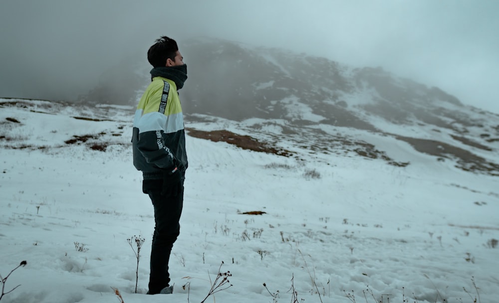 Hombre con chaqueta verde y negra y pantalones negros de pie en suelo cubierto de nieve