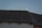A dark roof with corrugated tiles and a silhouette of a bird perched near the edge against a pale sky. The moon is rising in the background, creating a serene silhouette effect with the bird in front of it.