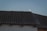 A dark roof with corrugated tiles and a silhouette of a bird perched near the edge against a pale sky. The moon is rising in the background, creating a serene silhouette effect with the bird in front of it.