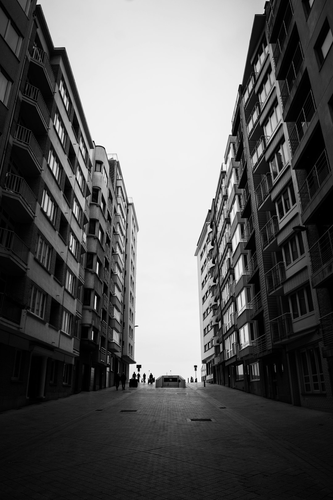 grayscale photo of people walking on street between high rise buildings