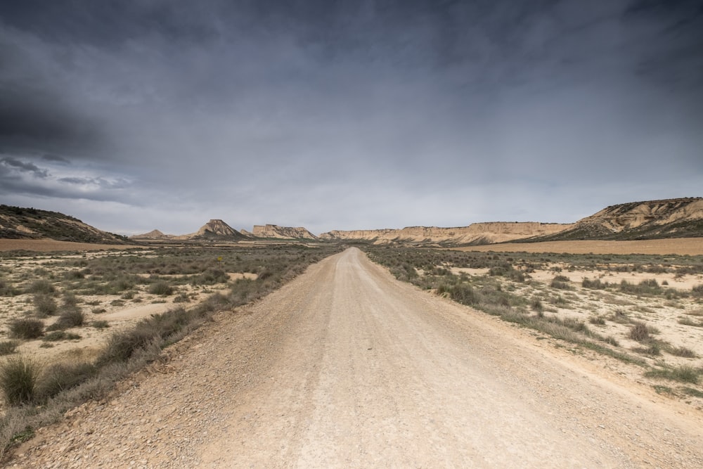 brown dirt road between green grass field under blue sky during daytime