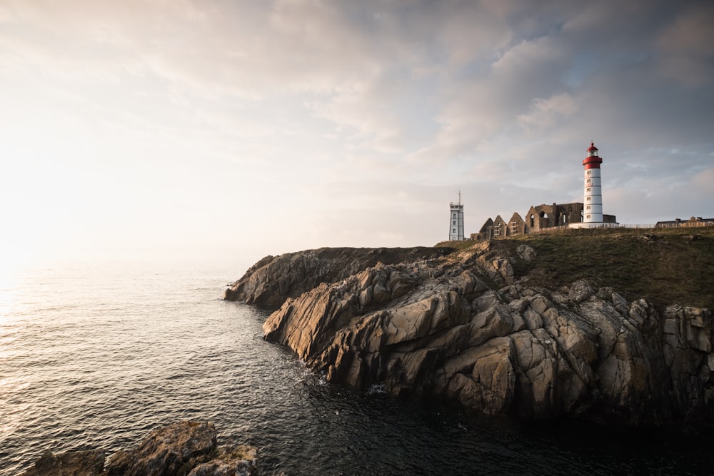 brown and white lighthouse on brown rock formation near body of water during daytime