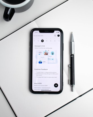 A Samsung smartphone resting on a modern desk beside a coffee cup and notebook.