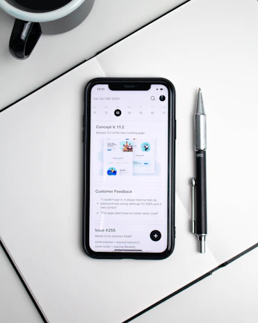A close-up of hands holding a smartphone displaying a helpful budgeting app, surrounded by notes and a cup of coffee.