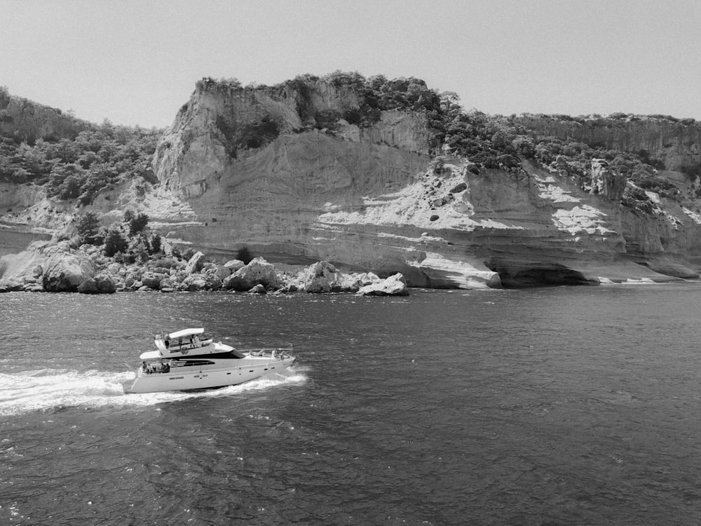 grayscale photo of white boat on sea near rock formation