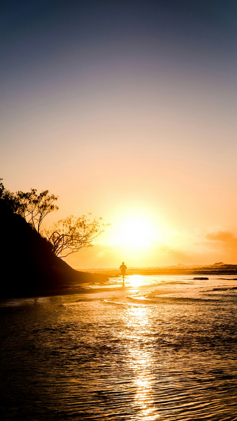 silhouette of person standing on seashore during sunset