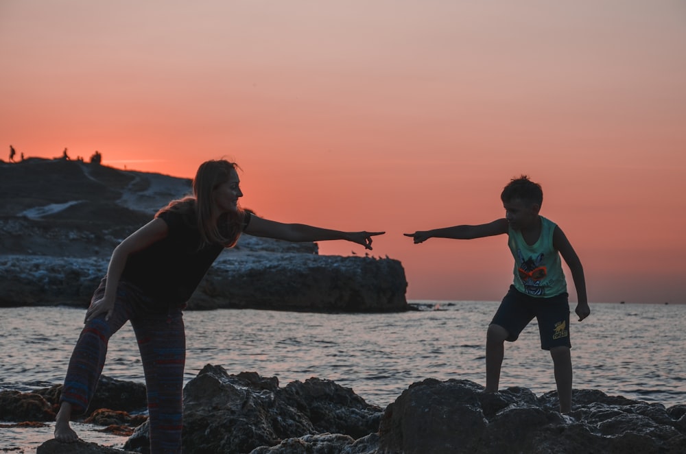 woman in black tank top and black leggings standing on rocky shore during sunset