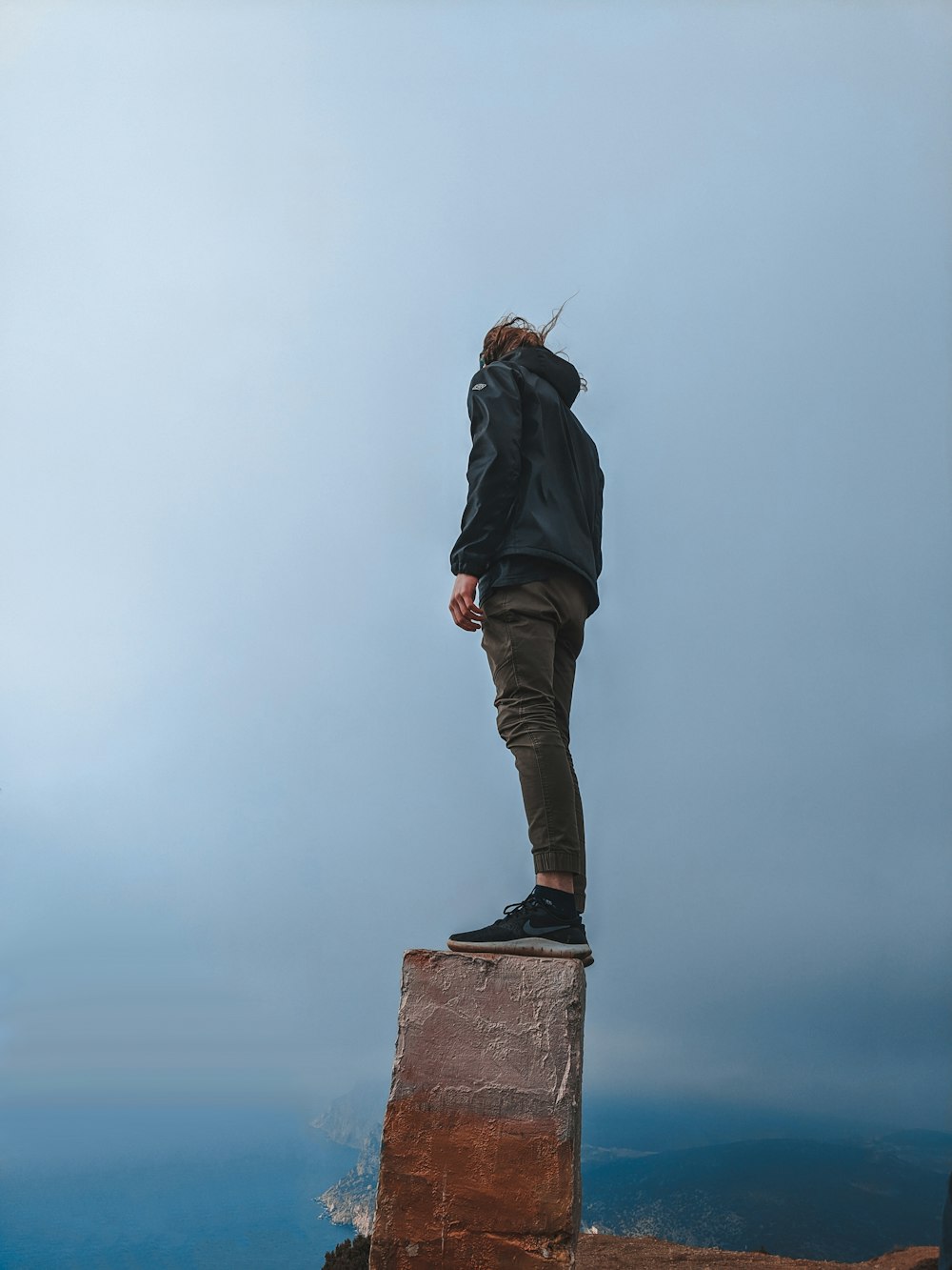 woman in black jacket and brown pants standing on rock