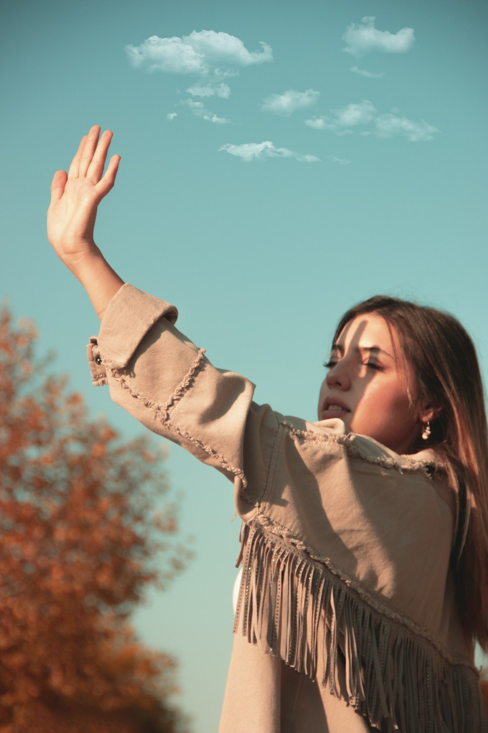 Mujer con camisa marrón de manga larga levantando la mano derecha