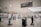 A largely empty airport terminal with rows of self-service kiosks. Overhead signage indicates directions to international arrivals and check-in areas. A person is cleaning the floor near a cart loaded with cleaning supplies. The atmosphere is quiet and unhurried.