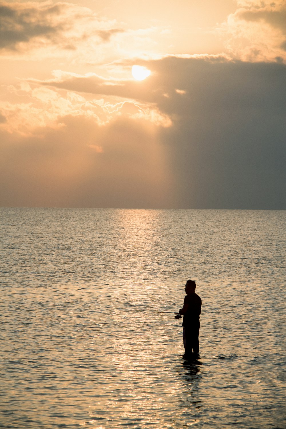 silhouette of man standing on sea shore during sunset