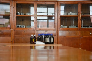 A wooden cabinet with glass doors contains various scientific instruments. In front of the cabinet, there are several brown bottles with blue and white caps placed on a wooden surface.