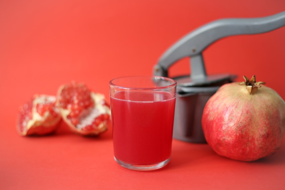 verre à boire transparent avec un liquide rouge à côté de la pomme rouge